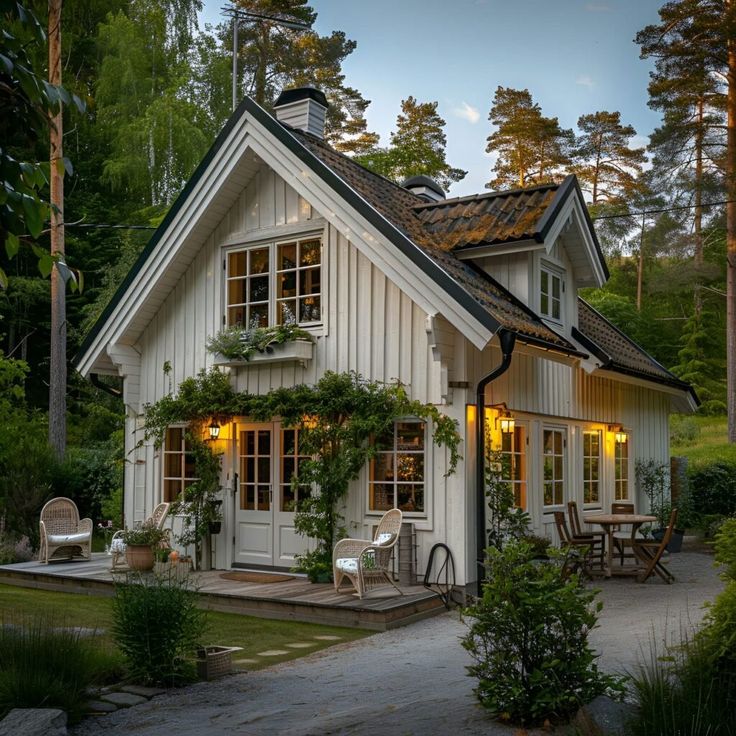 a small white house with lots of windows and plants on the front door, surrounded by greenery