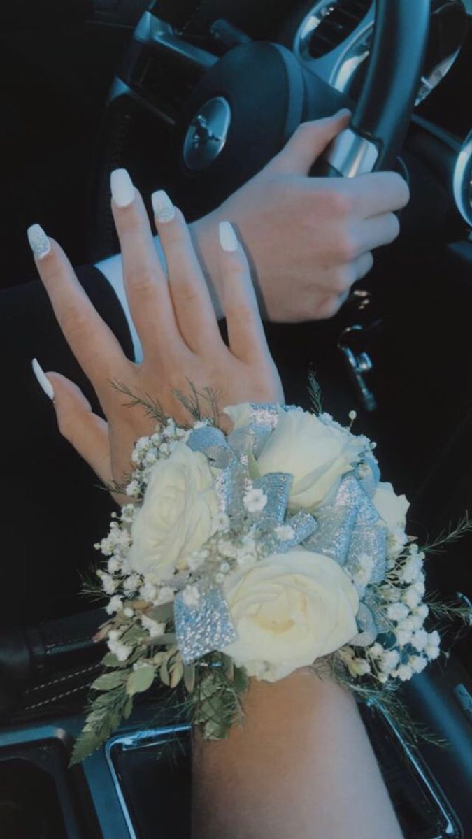 a woman's hand on the steering wheel of a car with white flowers and greenery