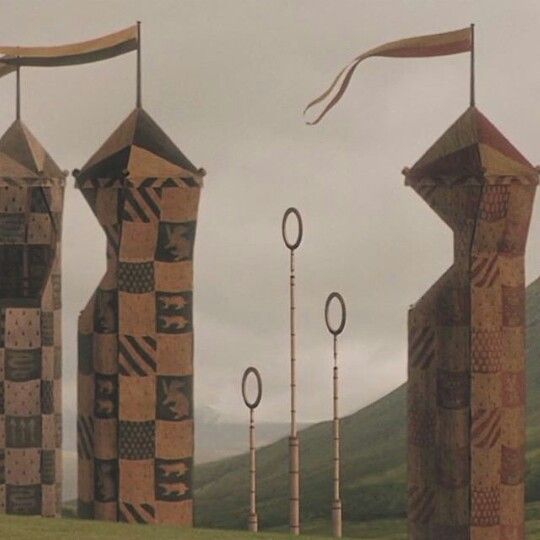 several tall sculptures in the middle of a grassy field with mountains in the background and cloudy sky