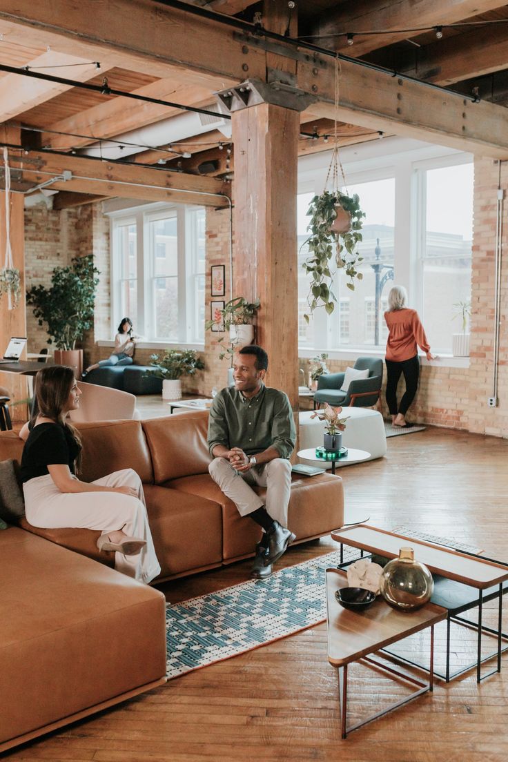 two people sitting on couches in an open room with wood floors and exposed ceilings