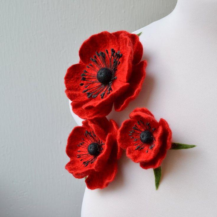 three red flowers are placed on top of a white mannequin's torso