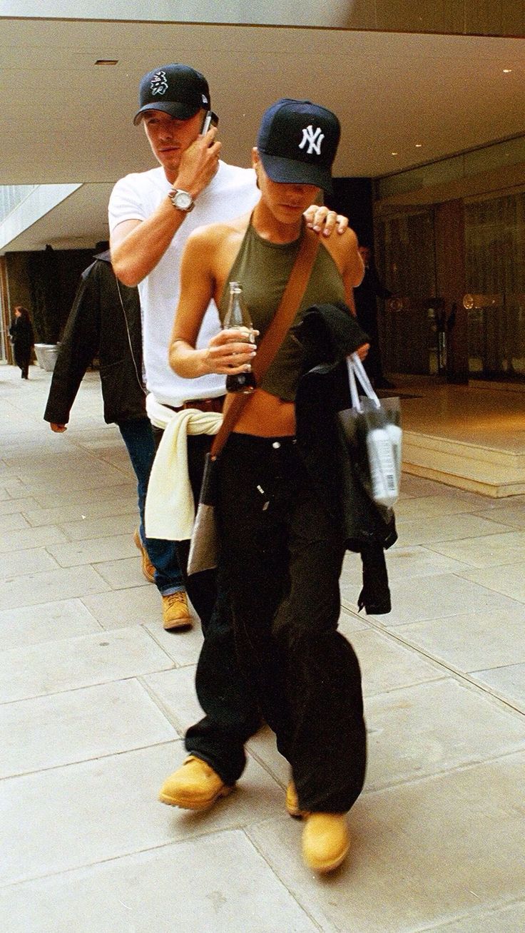 two men walking down the street talking on their cell phones and one holding a drink in his hand