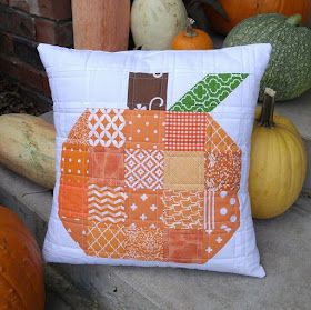 an orange patchwork pillow sitting on the ground next to pumpkins