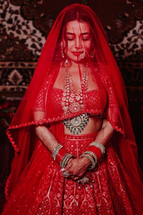 a woman in a red bridal gown with jewelry on her chest and hands behind her back