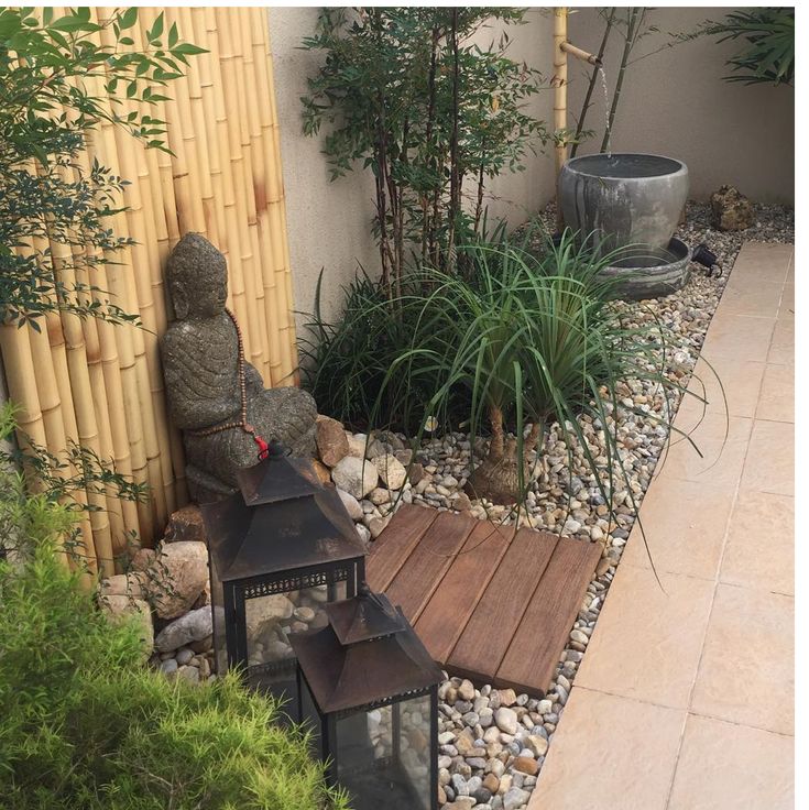 a small garden with rocks, plants and a buddha statue in the corner next to a bamboo fence