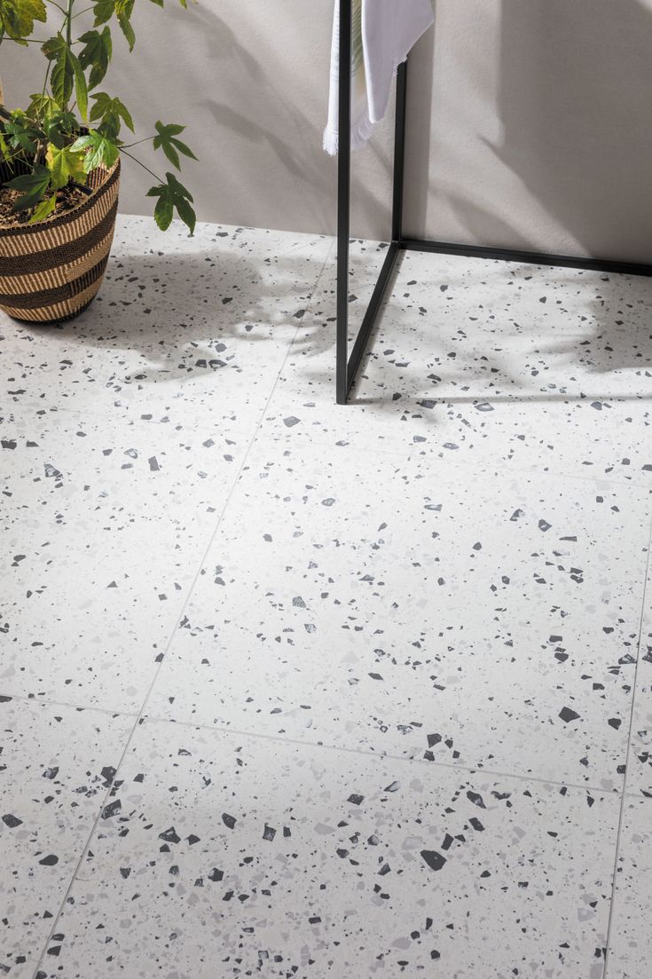 a bathroom with white and black speckles on the floor next to a potted plant