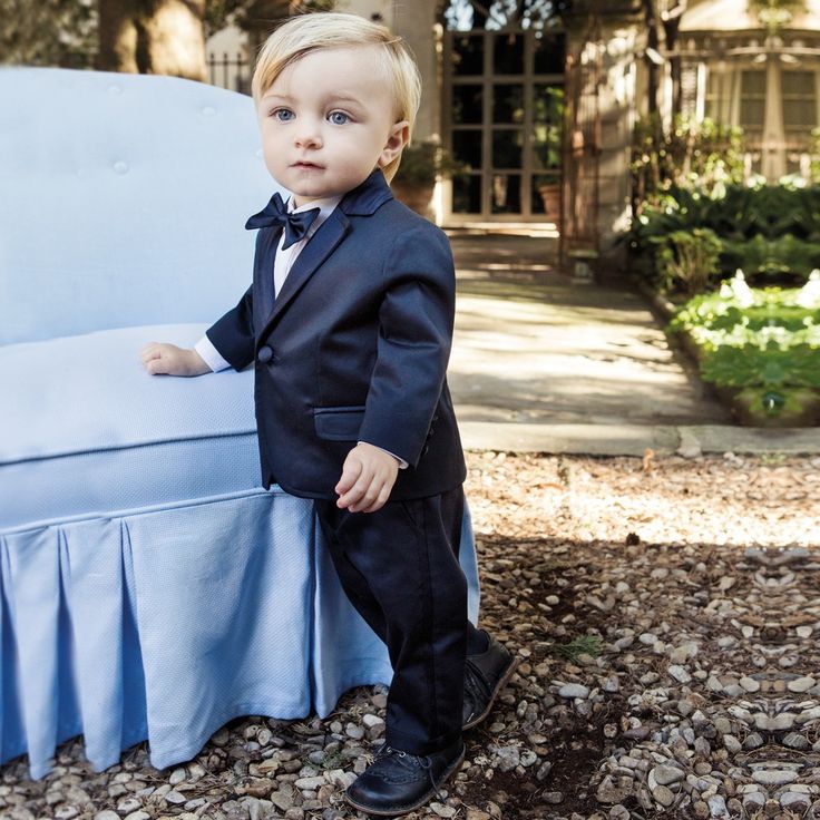 a little boy in a suit standing next to a blue couch