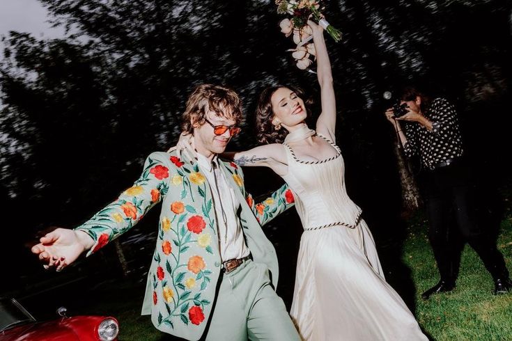 a man and woman are dancing in front of a red car