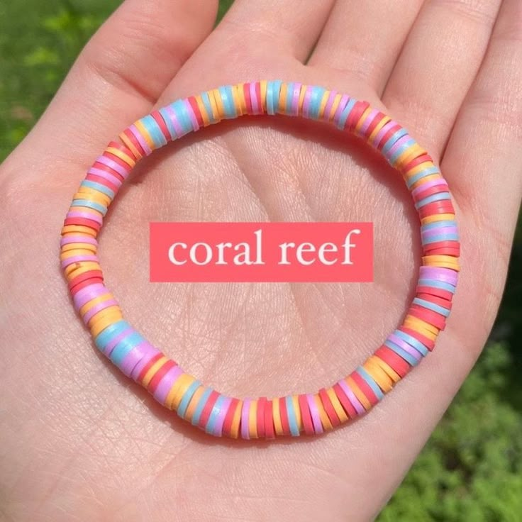 a hand holding a colorful bracelet with the word coral reef in it's center