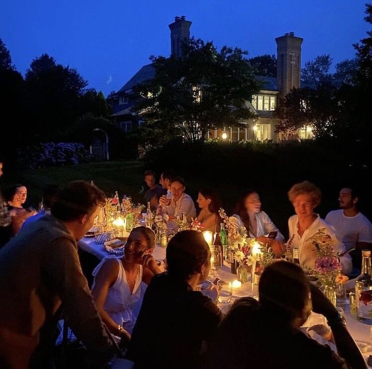 a group of people sitting around a dinner table with candles in front of their faces