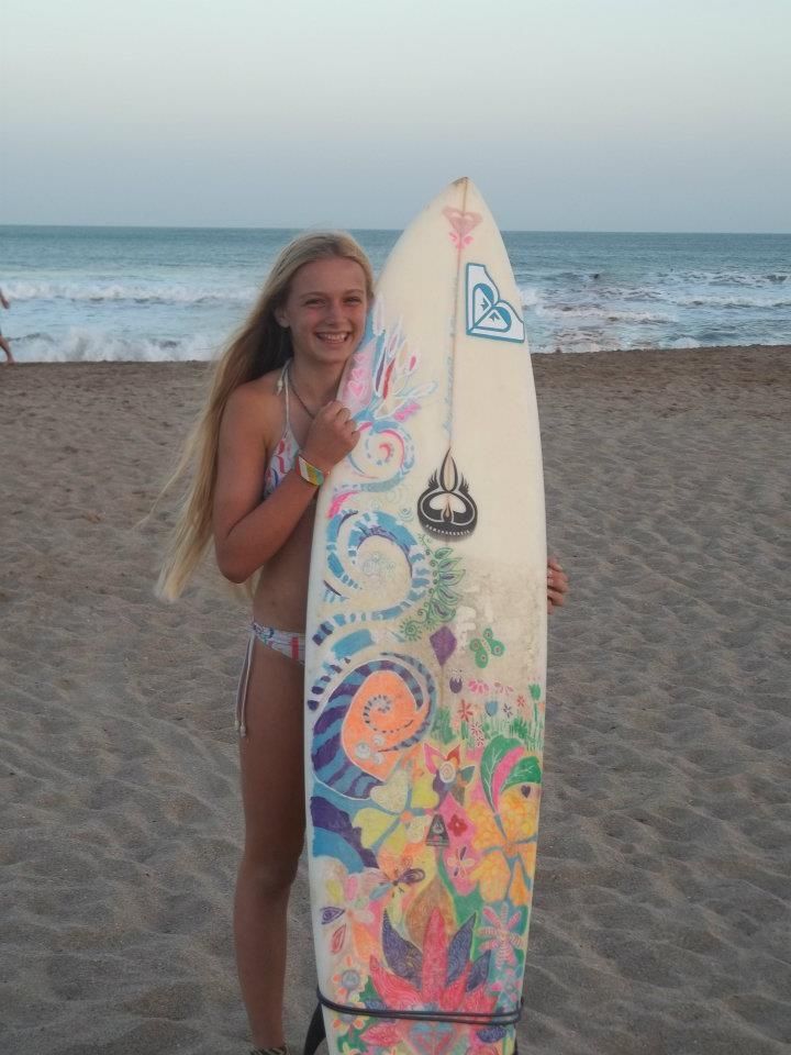 a woman holding a surfboard on top of a sandy beach next to the ocean