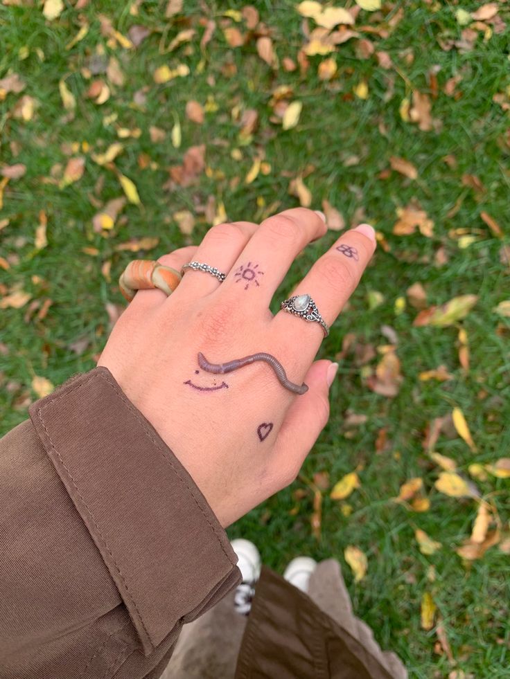 a person's hand with tattoos on it and two rings in the middle of their fingers