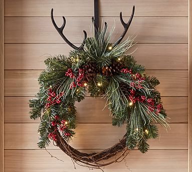 a christmas wreath hanging on the wall next to a door with lights and antlers