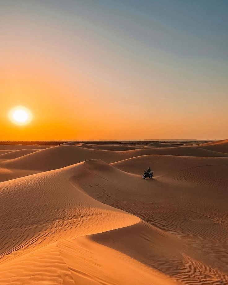 the sun is setting in the desert with sand dunes and people riding on their motorbikes