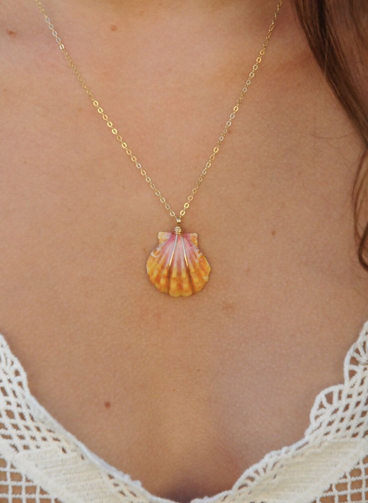 a woman wearing a necklace with an orange shell on it's back and gold chain