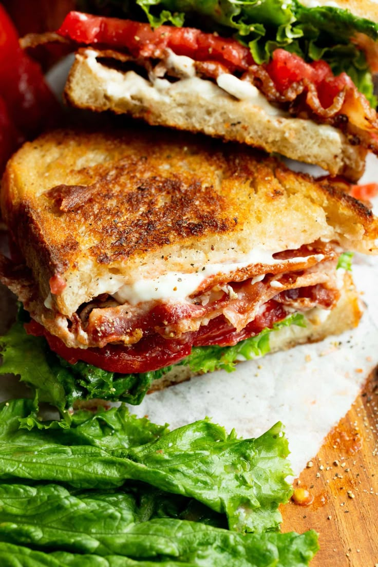 a sandwich cut in half sitting on top of a cutting board next to tomatoes and lettuce