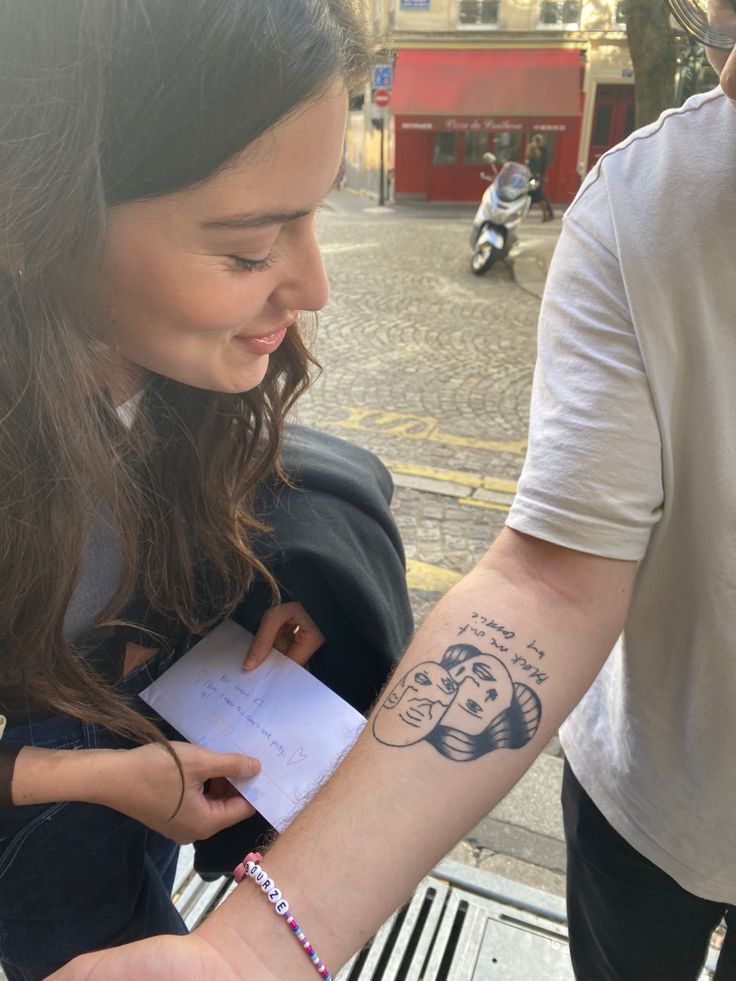 a woman with a tattoo on her arm holding onto a man's hand while he is looking at something