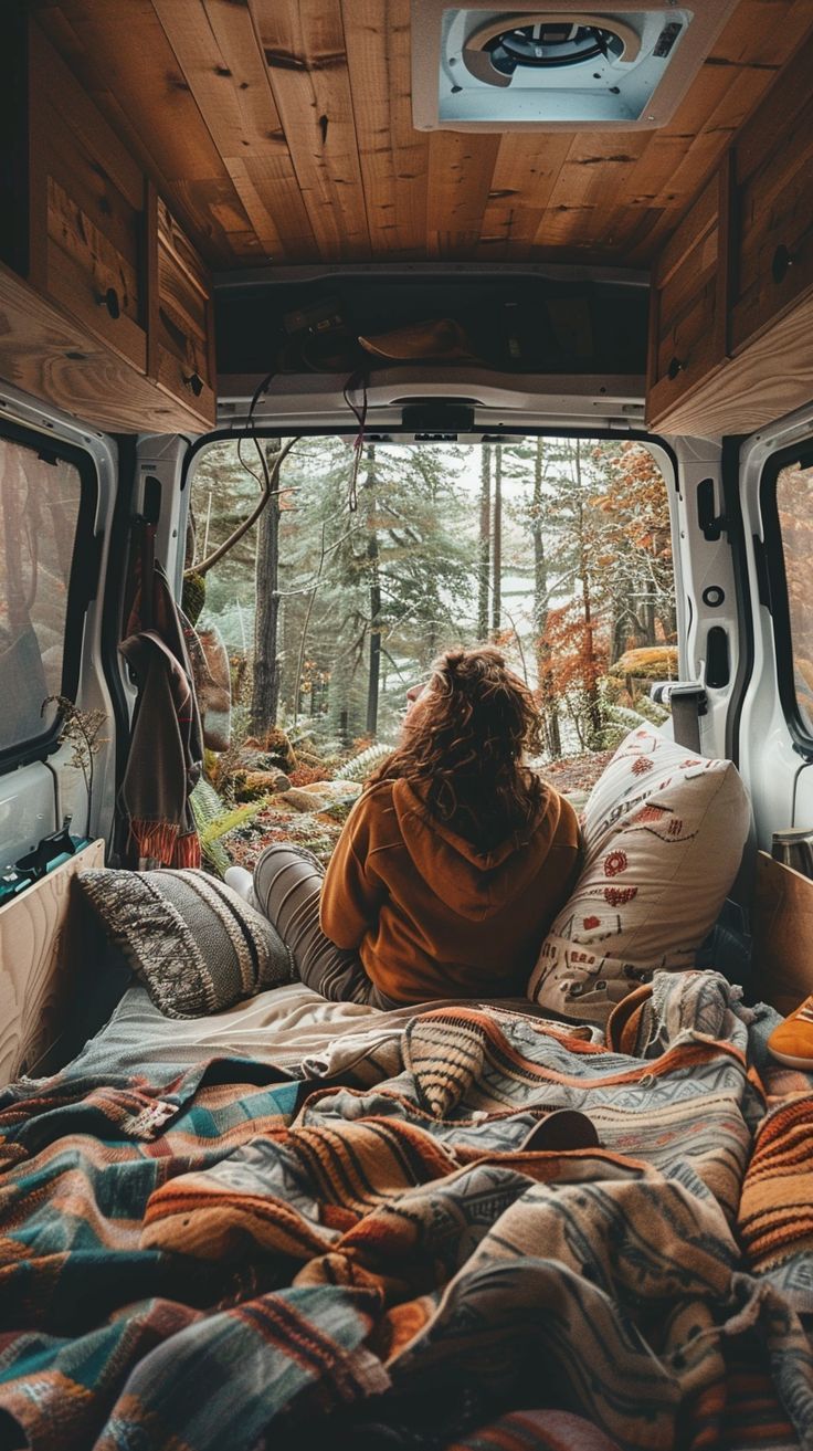 a woman sitting in the bed of an rv looking out the window at the woods