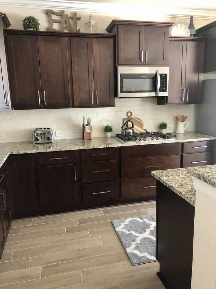 a kitchen with dark wood cabinets and granite counter tops, white appliances and gray rug