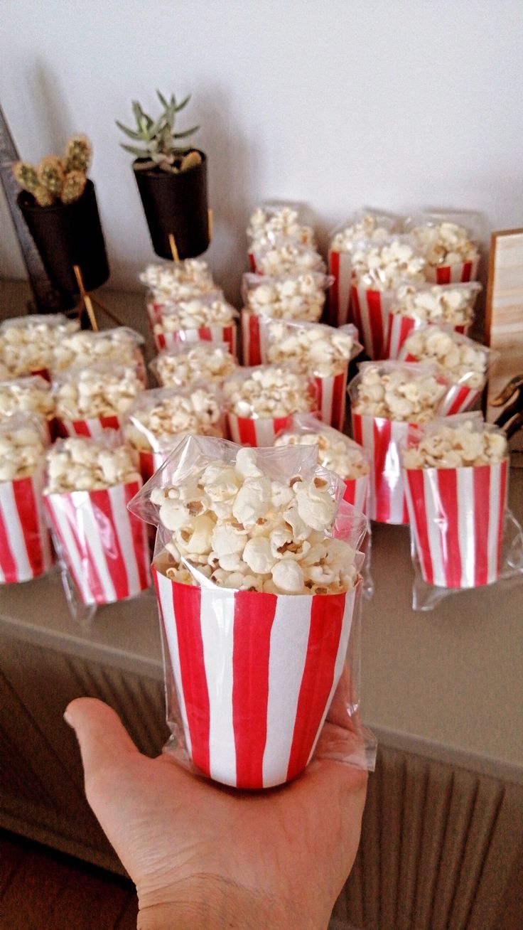 a person holding up a bag of popcorn in front of a table full of small cupcakes