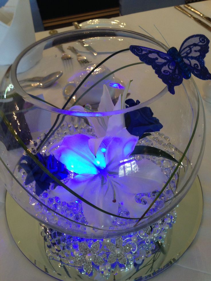 a glass bowl filled with flowers and butterflies on top of a white tablecloth covered table