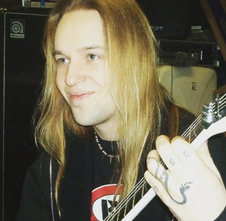 a man with long hair holding a guitar in his right hand and looking at the camera