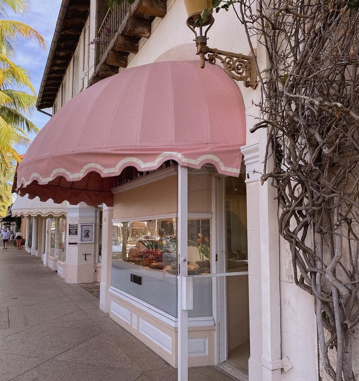 a pink awning on the side of a building next to a sidewalk and palm trees