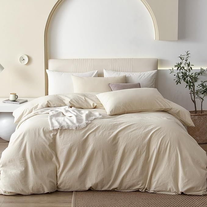 a bed with white linens and pillows in a neutral bedroom, next to a potted plant