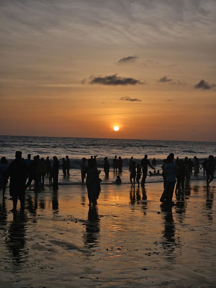 a group of people standing on top of a beach next to the ocean at sunset