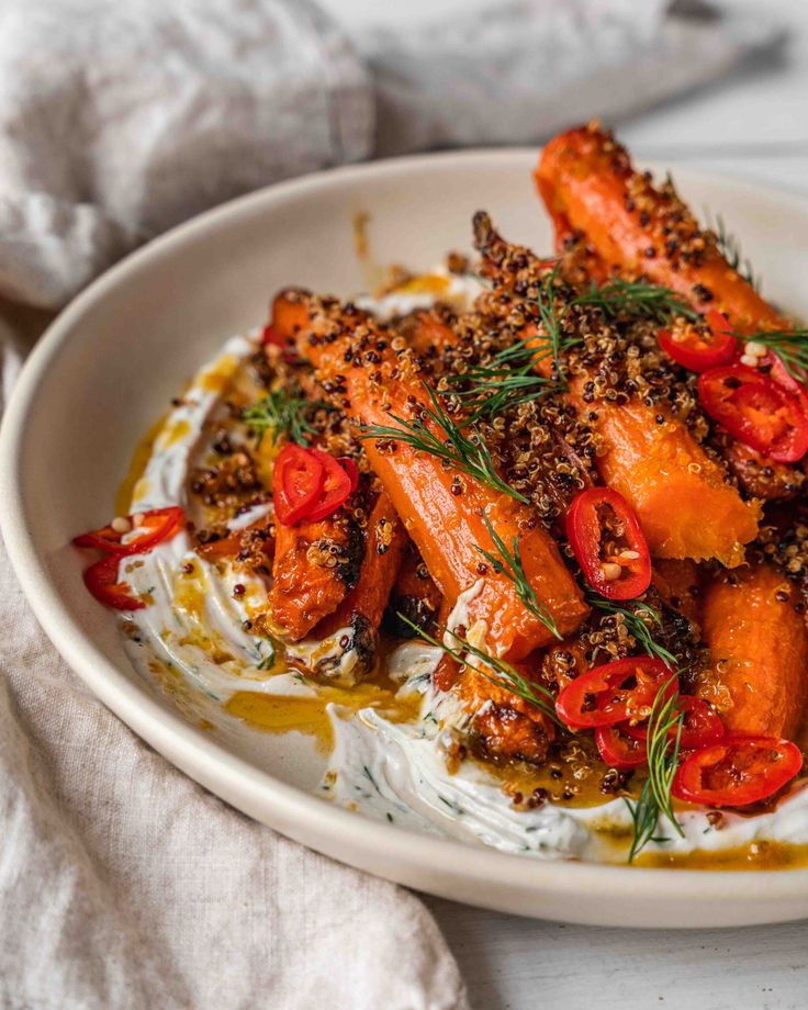 a white plate topped with carrots covered in sauce and sprinkled with herbs