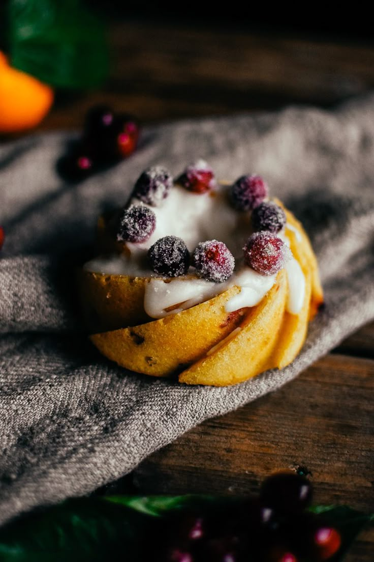 a pastry with icing and cranberries sitting on top of a table next to oranges