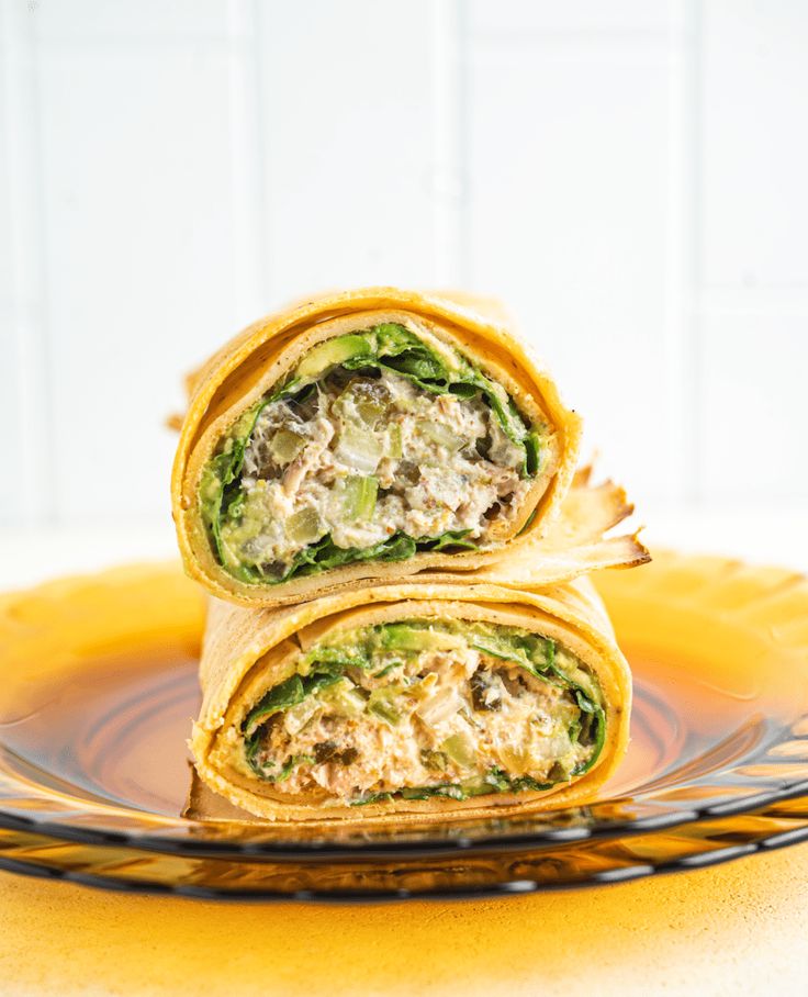 two wraps stacked on top of each other sitting on a yellow plate with a white tile background