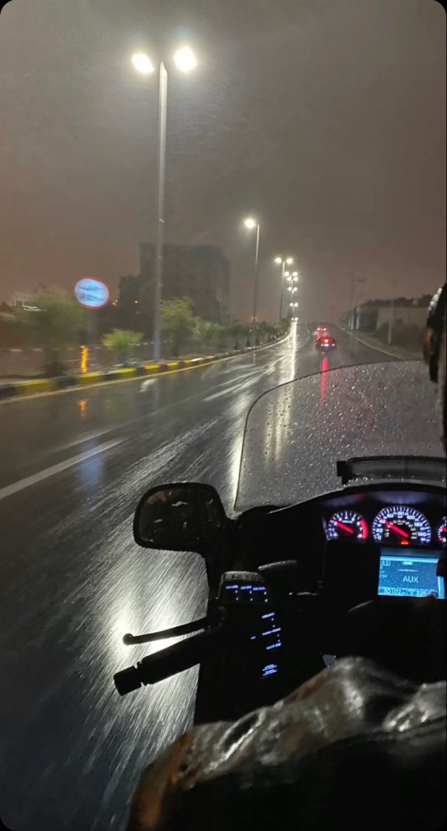 a motorcycle driving down a rain soaked road at night with street lights in the background