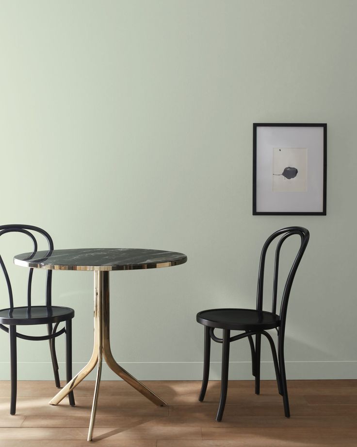 two chairs and a table in front of a white wall with a black framed picture on it