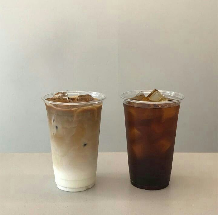 two drinks sitting next to each other on top of a white table with ice and brown liquid