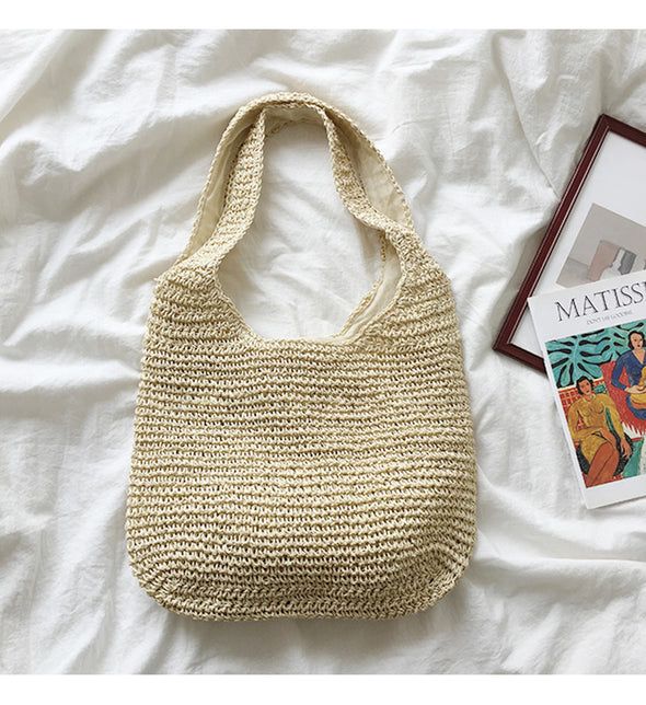 a white purse sitting on top of a bed next to a book and magazine holder