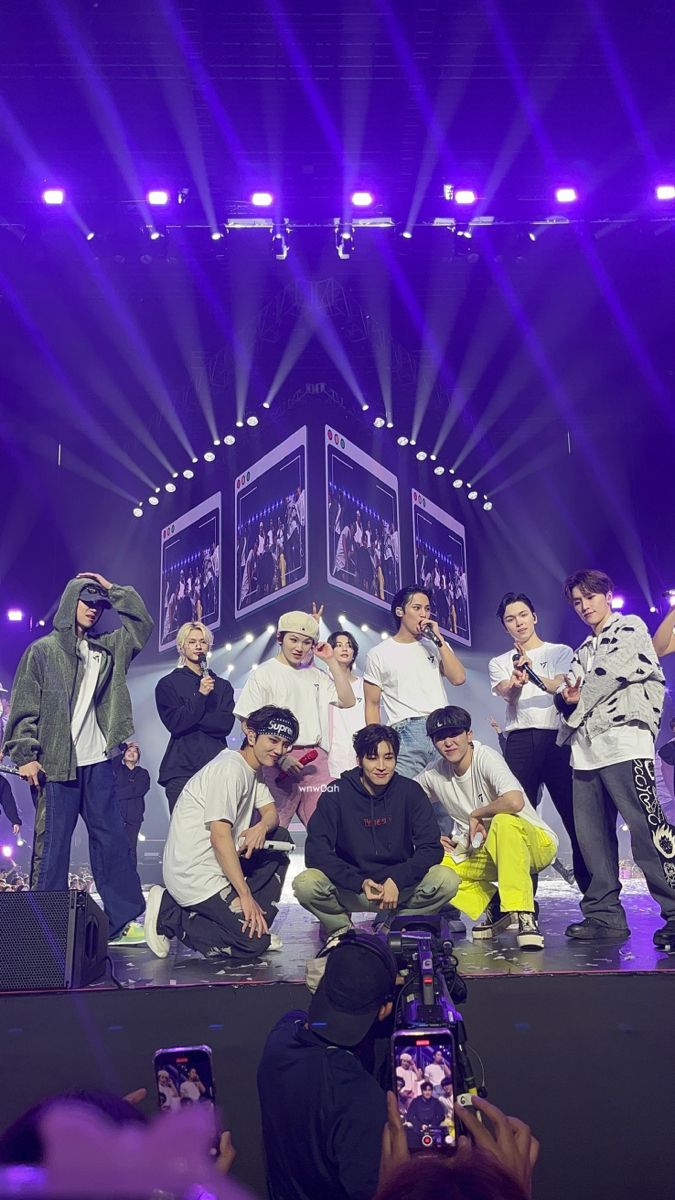 a group of young men standing on top of a stage with purple lights behind them