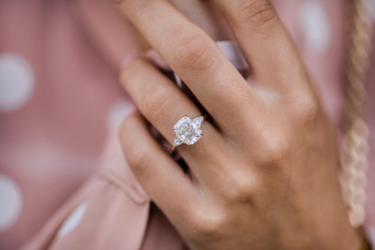 a woman's hand with a diamond ring on her finger and a pink polka dot shirt