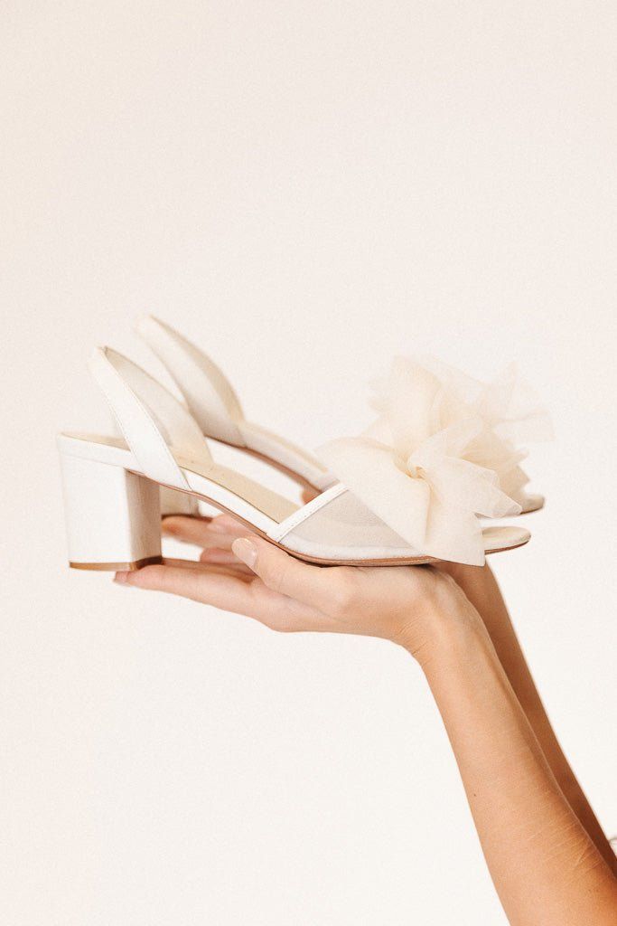 a woman's hand holding a pair of white high heeled shoes with flowers on them