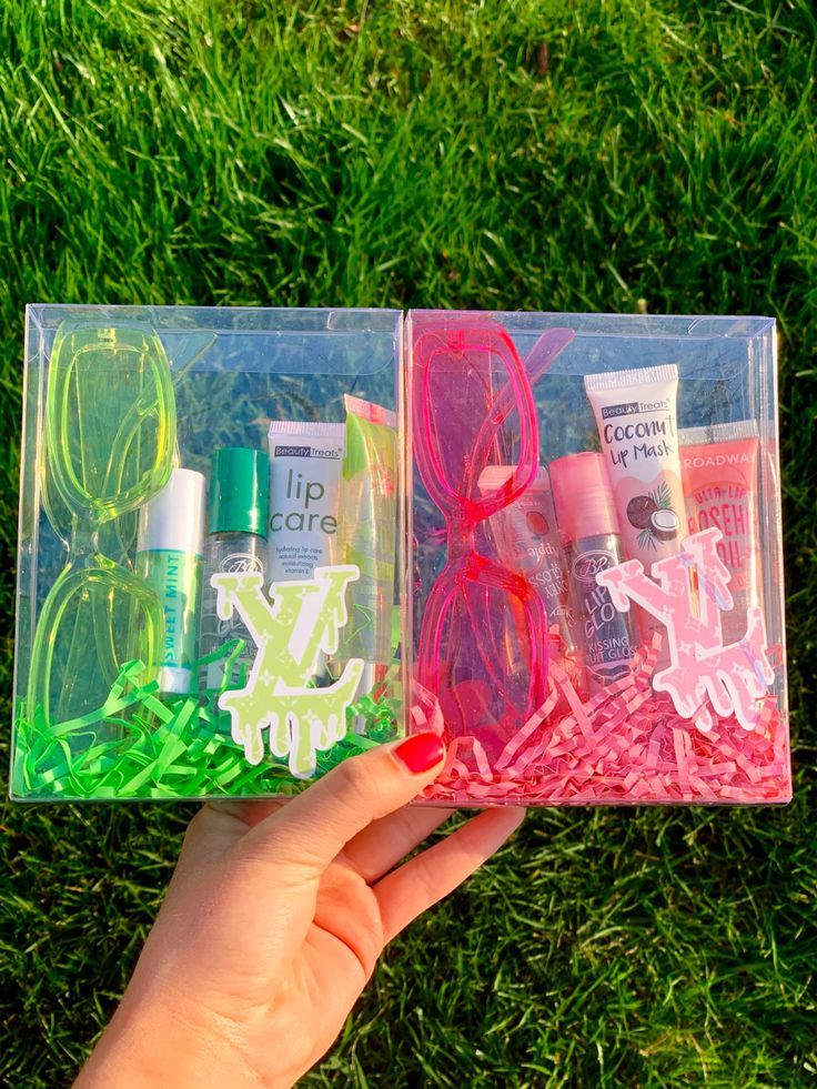 two clear plastic boxes filled with personal care items on top of green grass in front of someone's hand