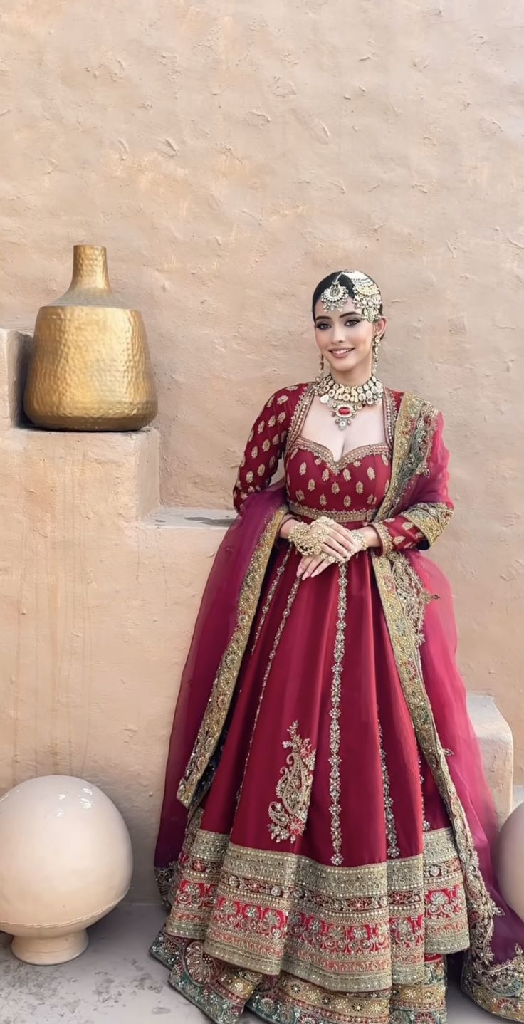 a woman in a red and gold wedding dress standing next to a vase with flowers on it