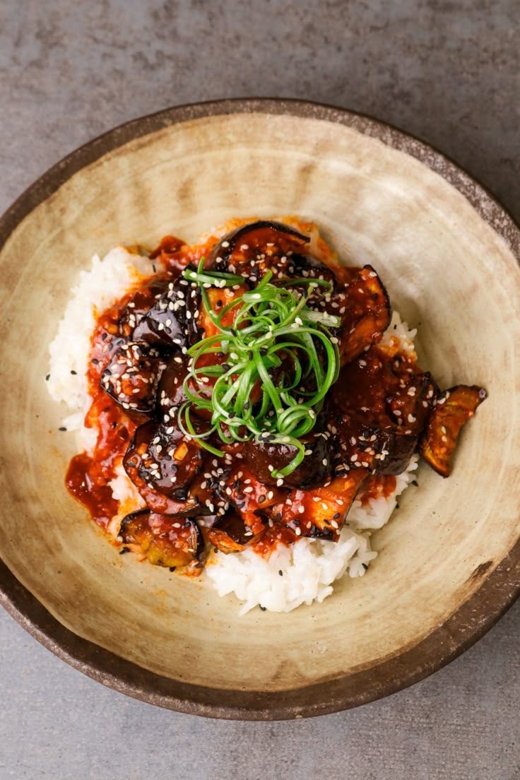 a bowl filled with rice and meat covered in sauce