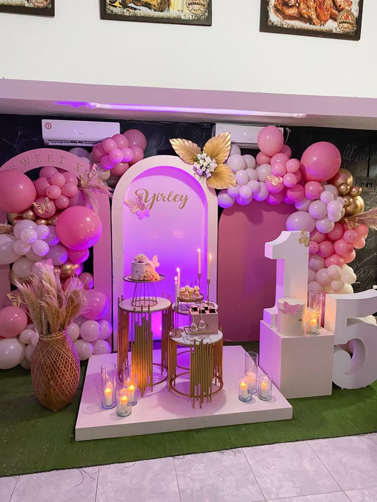 a pink and gold birthday party with balloons, candles, cake and decorations on display