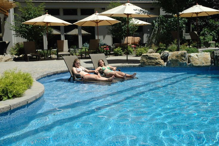 two women lounging on lounge chairs next to a swimming pool with umbrellas in the background