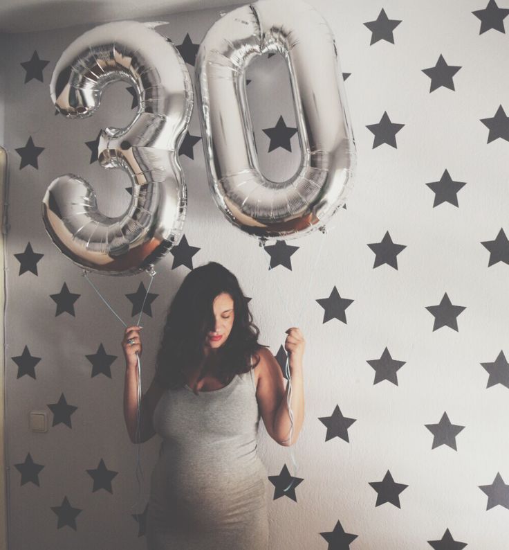 a pregnant woman holding balloons in front of a wall with stars on it and the number 30