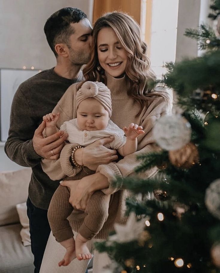 a man and woman holding a baby in front of a christmas tree