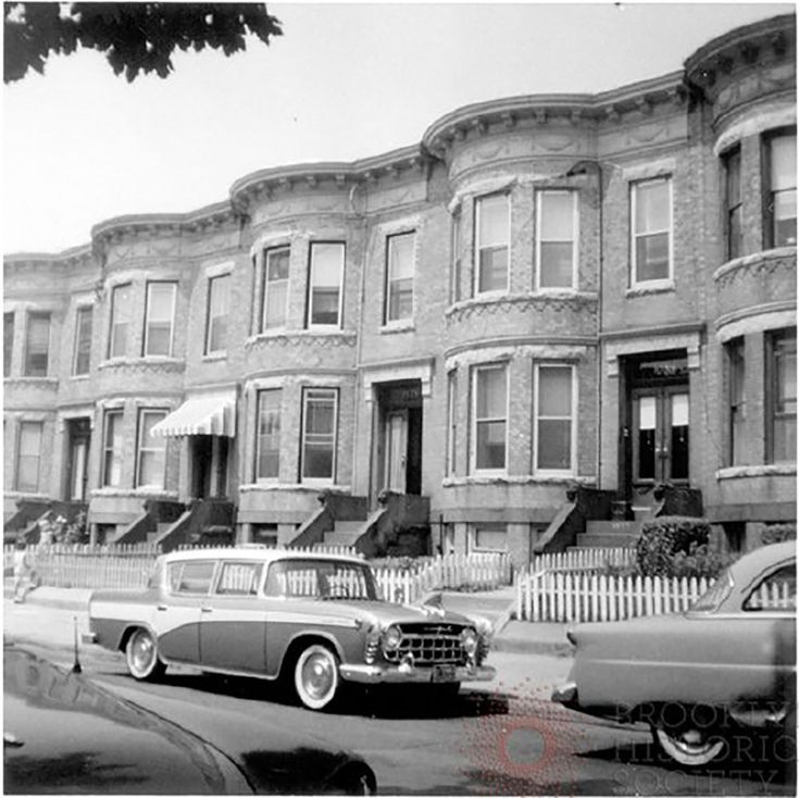 an old black and white photo of cars parked in front of row houses with balconies