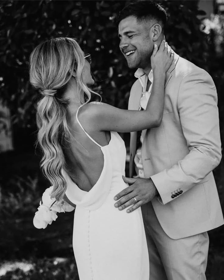 a man in a suit and woman in a white dress are smiling at each other