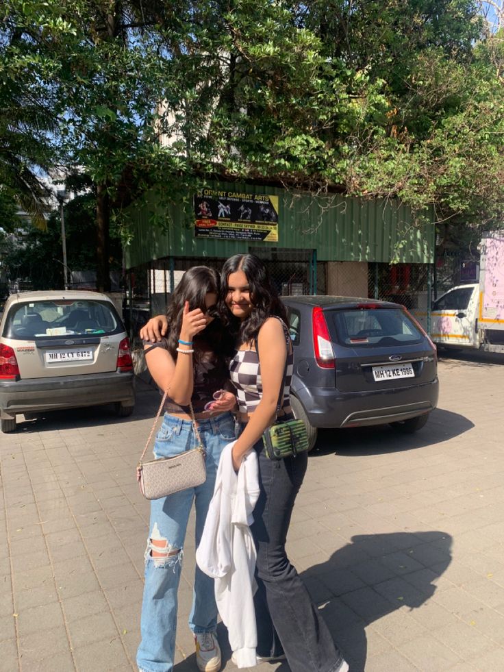 two women standing next to each other in front of parked cars