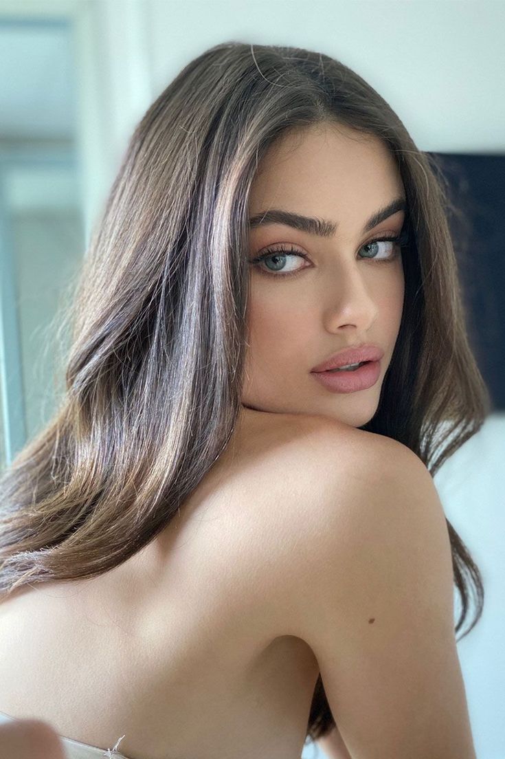 a woman with long brown hair and blue eyes is posing for the camera, wearing a strapless bra